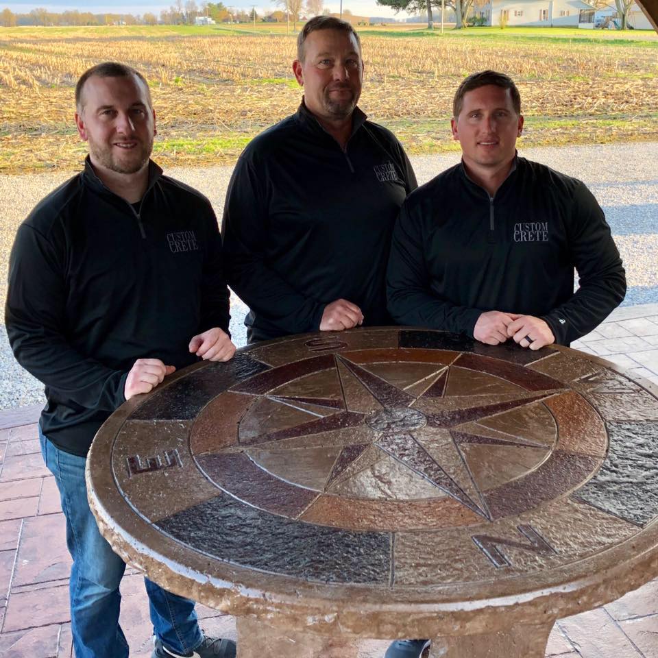 The Custom Crete team standing behind their stamped compass-star concrete table