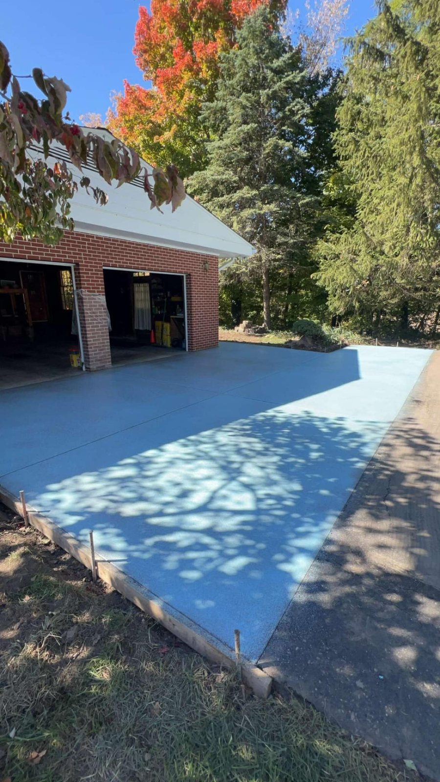 Fresh blue-gray tinted broom-finished concrete driveway at a brick garage.