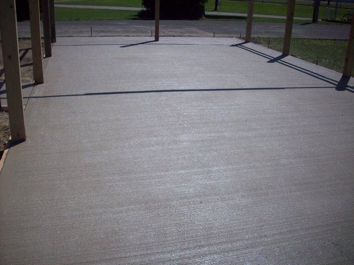 A finished broom-textured plain concrete pad bordered by wood posts in a yard setting.