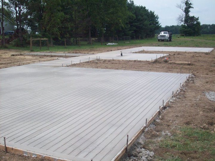 Broom-finished concrete slab still in wooden forms at a rural property with a pickup truck in back.