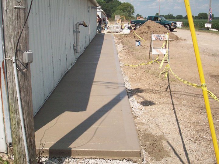 Long freshly finished tan concrete walkway running along the side of a large metal commercial building.