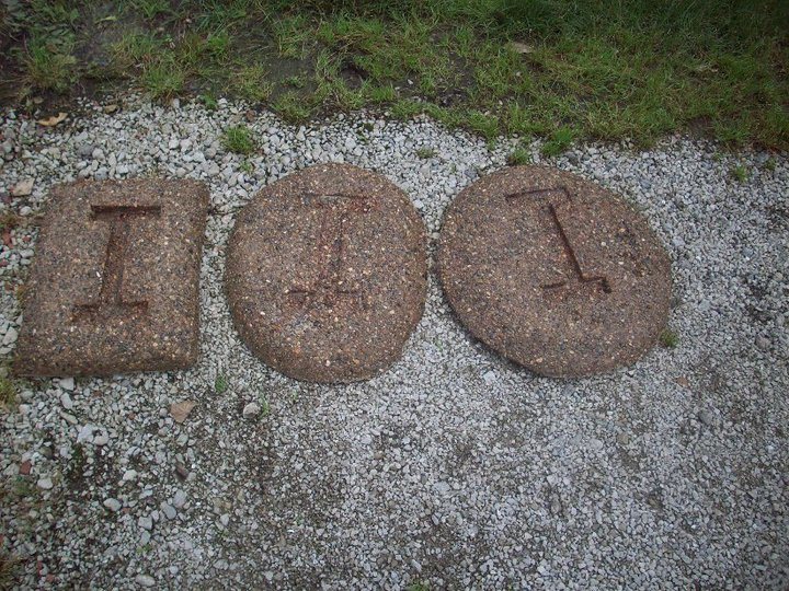 Three exposed-aggregate decorative stepping stones each imprinted with the letter I resting on gravel.