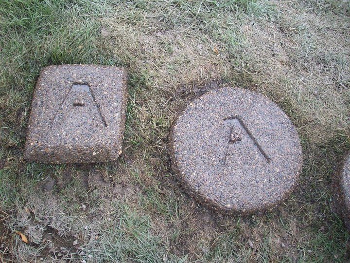 Two custom exposed-aggregate concrete stepping stones, one square and one round, each engraved with the letter A, set in grass.