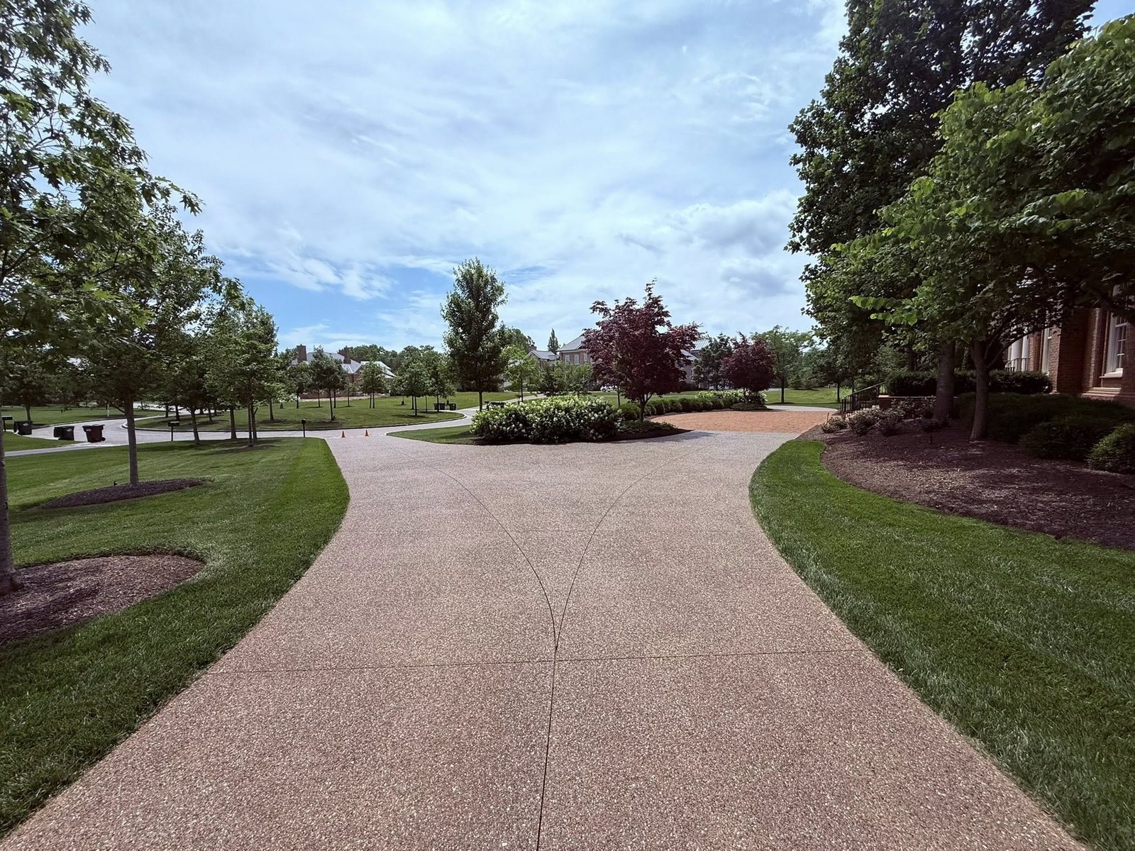 Tan exposed-aggregate concrete walkway winding through landscaped campus grounds.