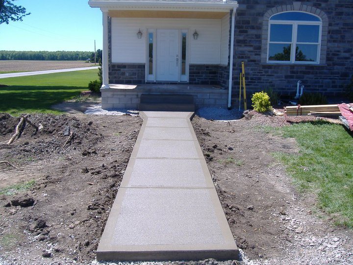 Exposed aggregate concrete walkway with a smooth tan border leading to a stone home's front porch.
