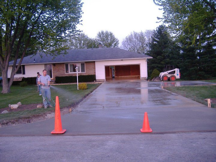 Newly finished plain concrete residential driveway, still wet and cordoned with cones, leading to an attached garage.
