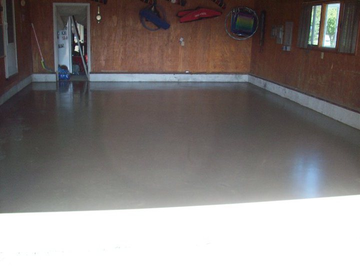 A newly poured and finished smooth gray concrete garage slab inside a wood-paneled garage with the old floor now replaced.