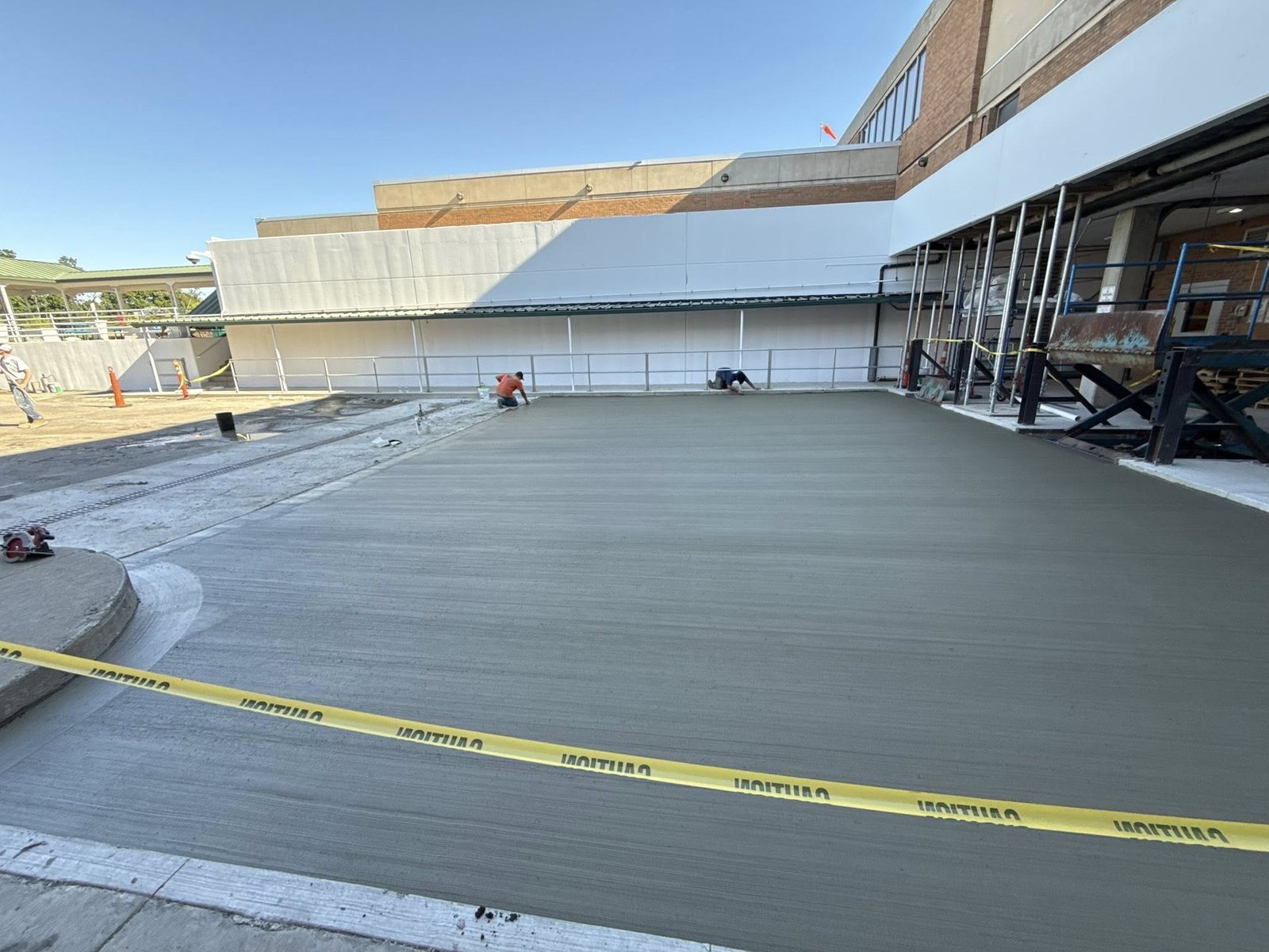 Large smooth commercial concrete slab being finished behind a brick building.