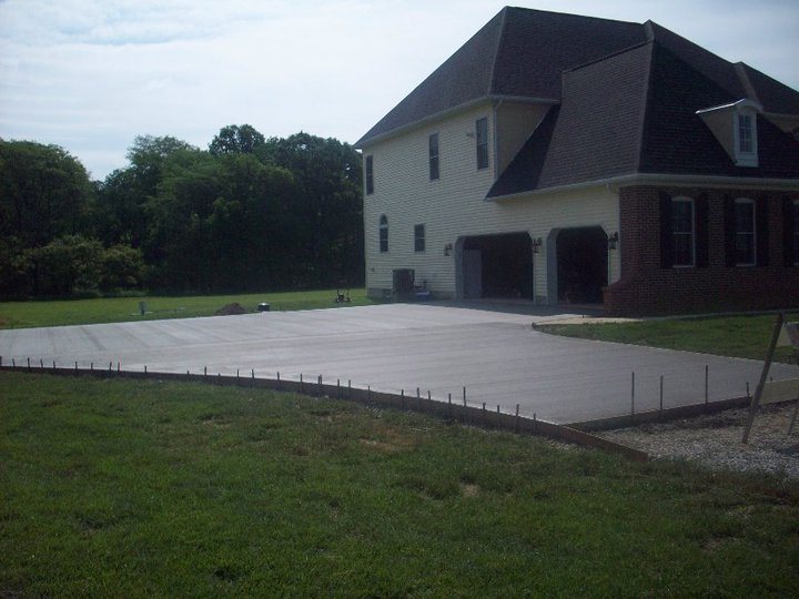 A large finished plain concrete driveway and parking apron in front of a two-story home's three-car garage.