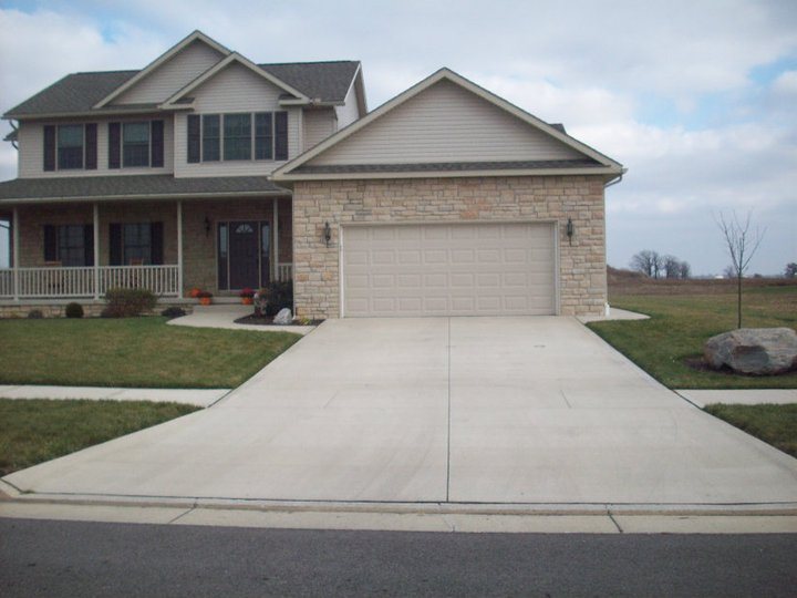 A long finished plain concrete driveway approaching the attached garage of a two-story stone-and-siding home.