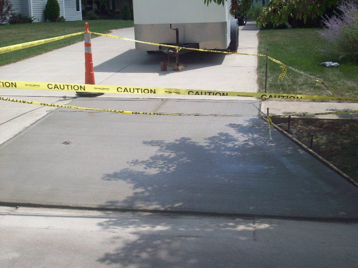 Freshly poured driveway extension cordoned off with caution tape while curing at a residential home.