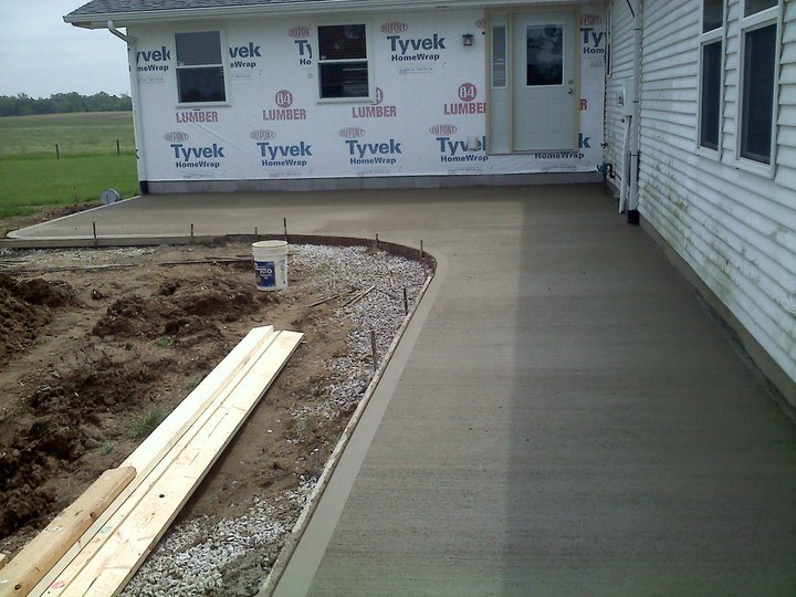 Newly poured plain broom-finished concrete patio behind a house still wrapped in Tyvek house wrap.