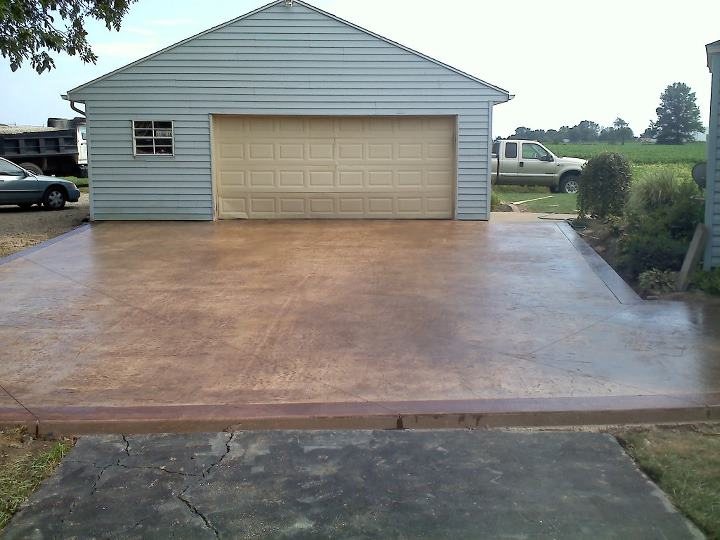 A tan stained and textured concrete driveway with a brown stamped border in front of a detached garage.