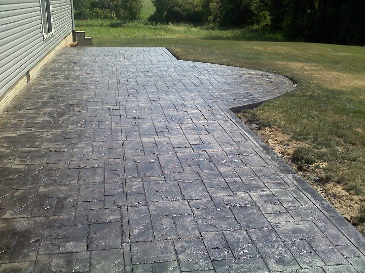 A large charcoal ashlar-pattern stamped concrete patio with a curved edge wrapping around the side of a house.