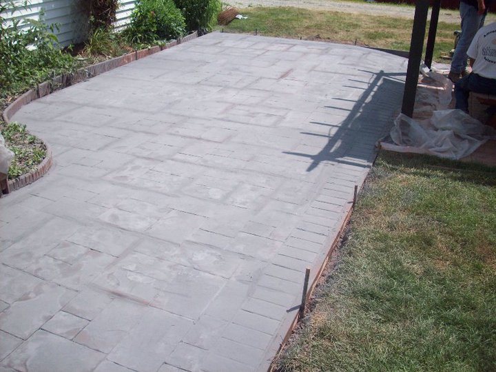 A finished gray stamped concrete patio with an ashlar slate tile pattern and brick-edge border in a backyard.