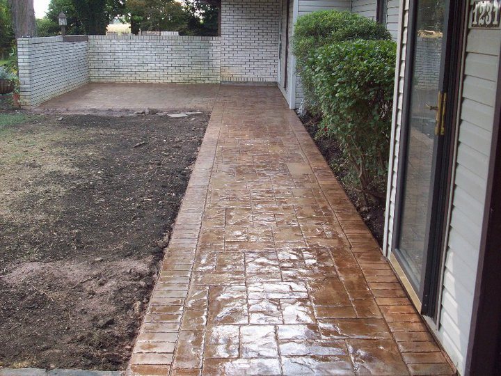 A wet-sealed stamped ashlar-pattern colored concrete walkway leading to a patio along a brick home.