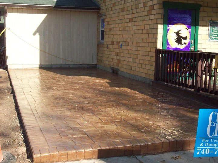 Finished tan and brown stamped concrete patio with a running-bond brick pattern and brick border in a courtyard beside a commercial building.
