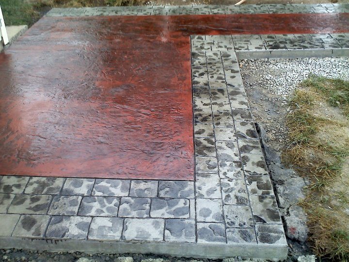 Close-up of a red-stained slate-textured stamped concrete patio bordered by gray cobblestone banding.