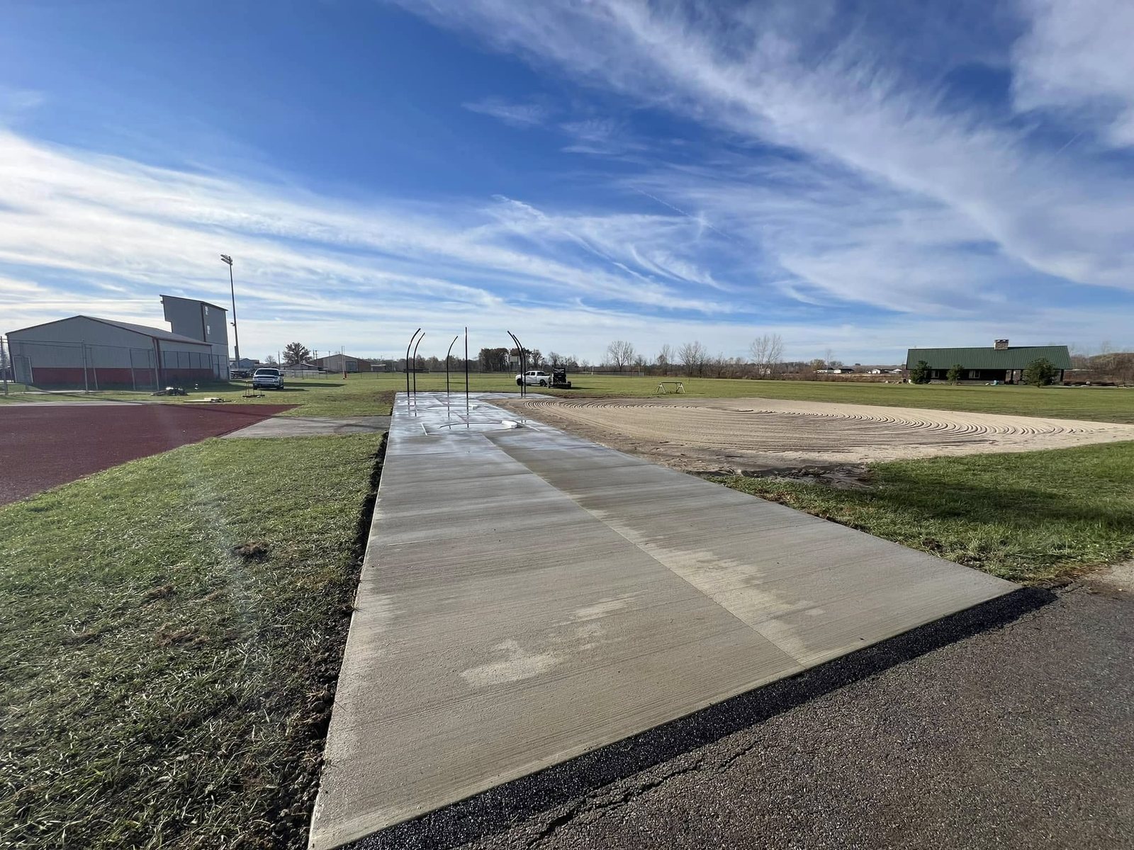 Long broom-finished concrete pole-vault runway at a school track facility.
