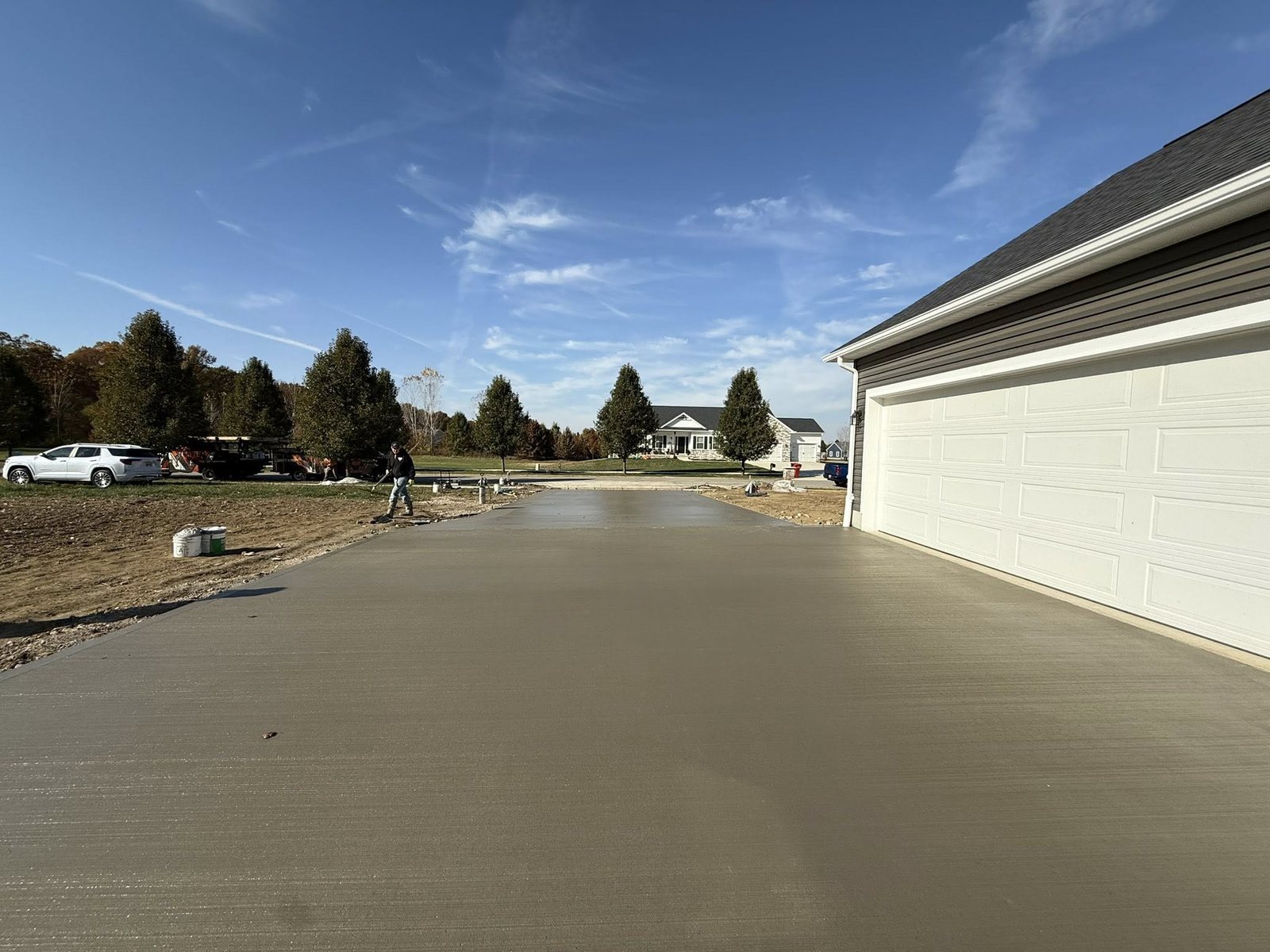 Wide freshly finished concrete driveway beside a home with white garage doors.