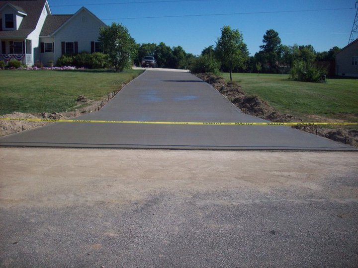 A finished plain gray residential concrete driveway with caution tape, freshly cured in front of a rural home.